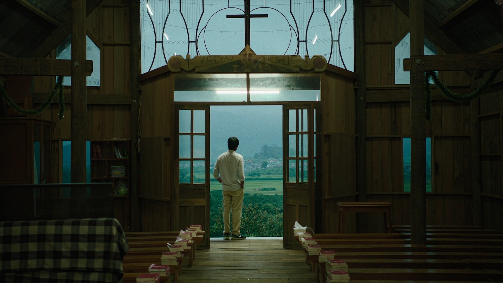 Inside the Yellow Cocoon Shell 2023_04_13-ITYCS-PRINT_02 A man stands with his hands in his pockets at the entrance of a church, with the doors open showing a verdant green landscape beyond