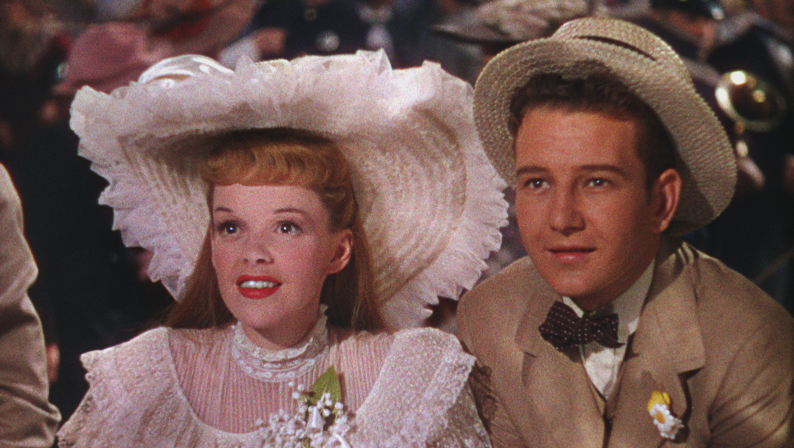 A young man and woman wearing turn of the century American upper-class outfits gaze longingly.