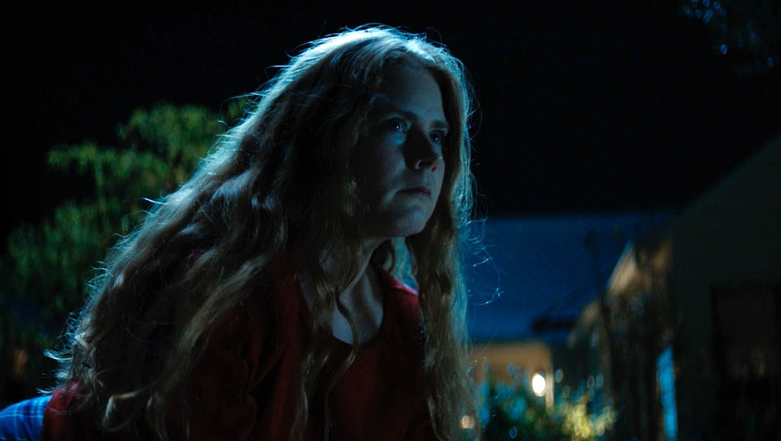 A woman in a red t-shirt crouches on all fours outside at night.