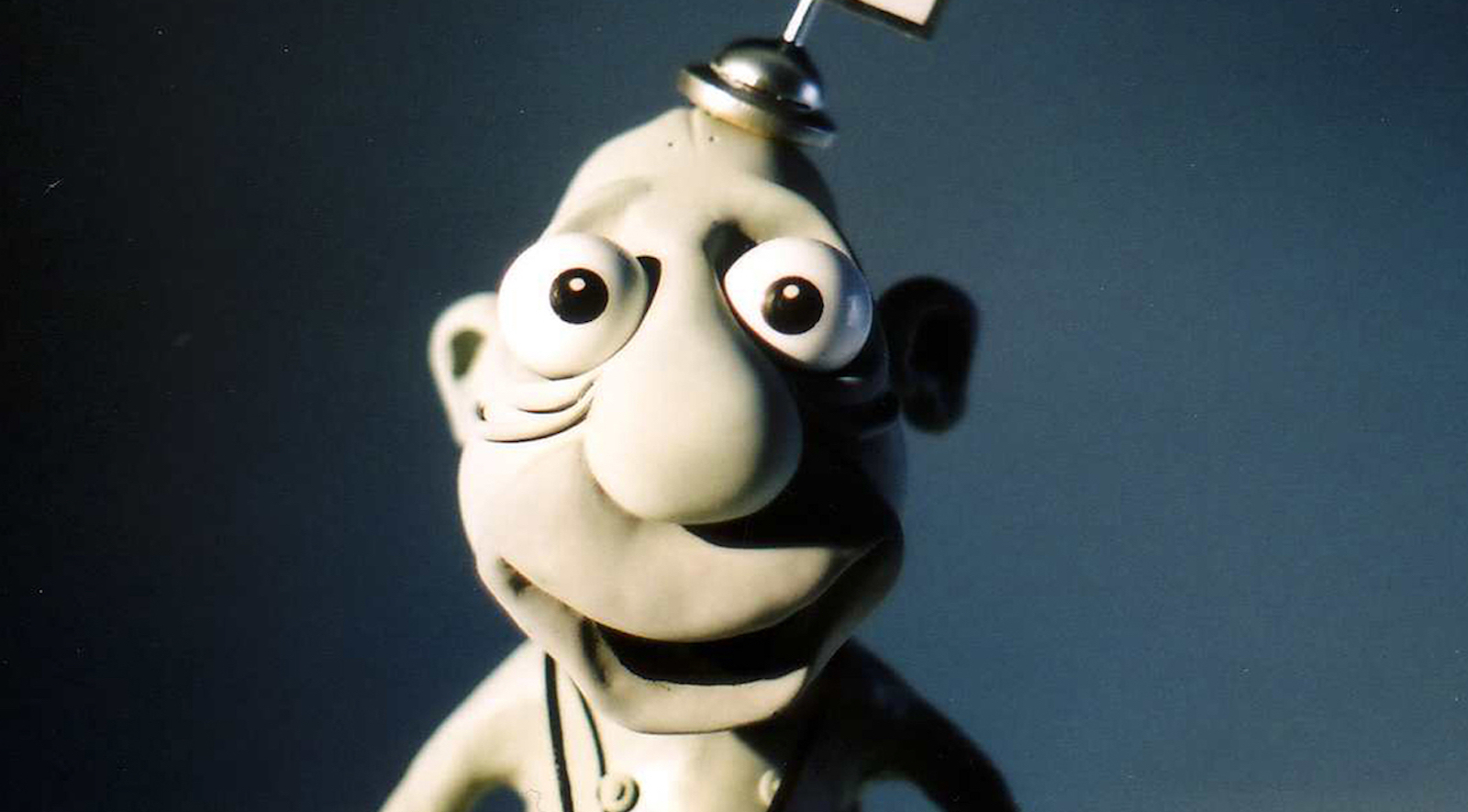 A claymation character with big bulging eyes and a goofy smile looks ahead at us.