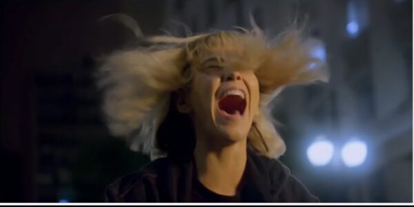 A woman with tousled blonde hair blowing in the wind screams with her mouth wide open.