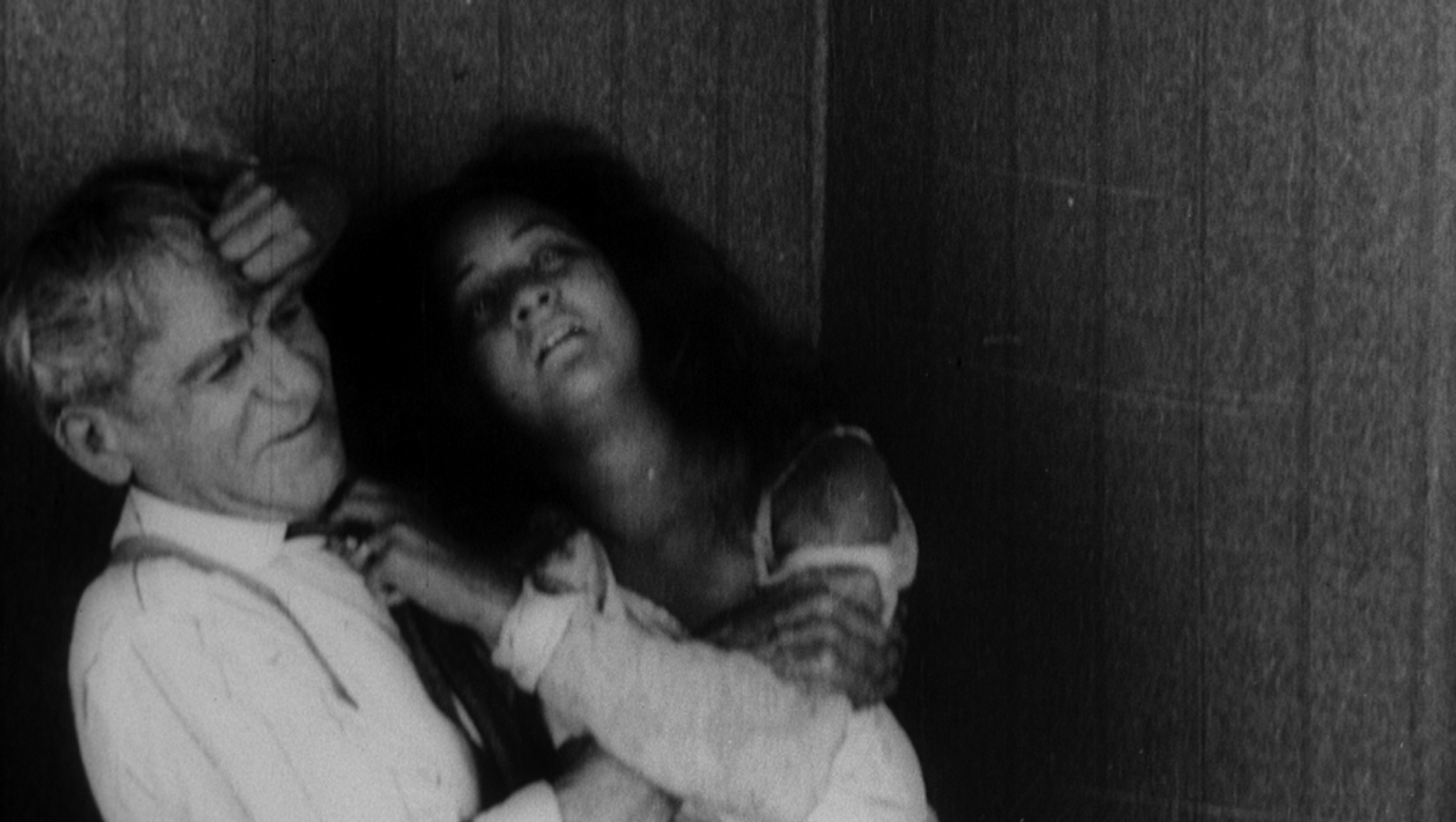 A woman with tattered dark hair places her hand passionately against an older man.