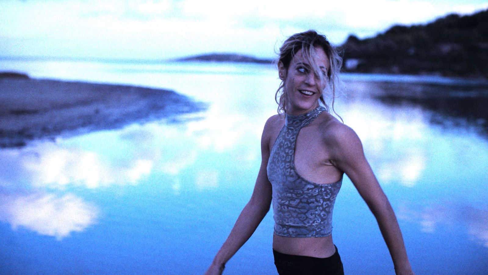 A woman in a tank top stands in front of a cool icy reflective pond.