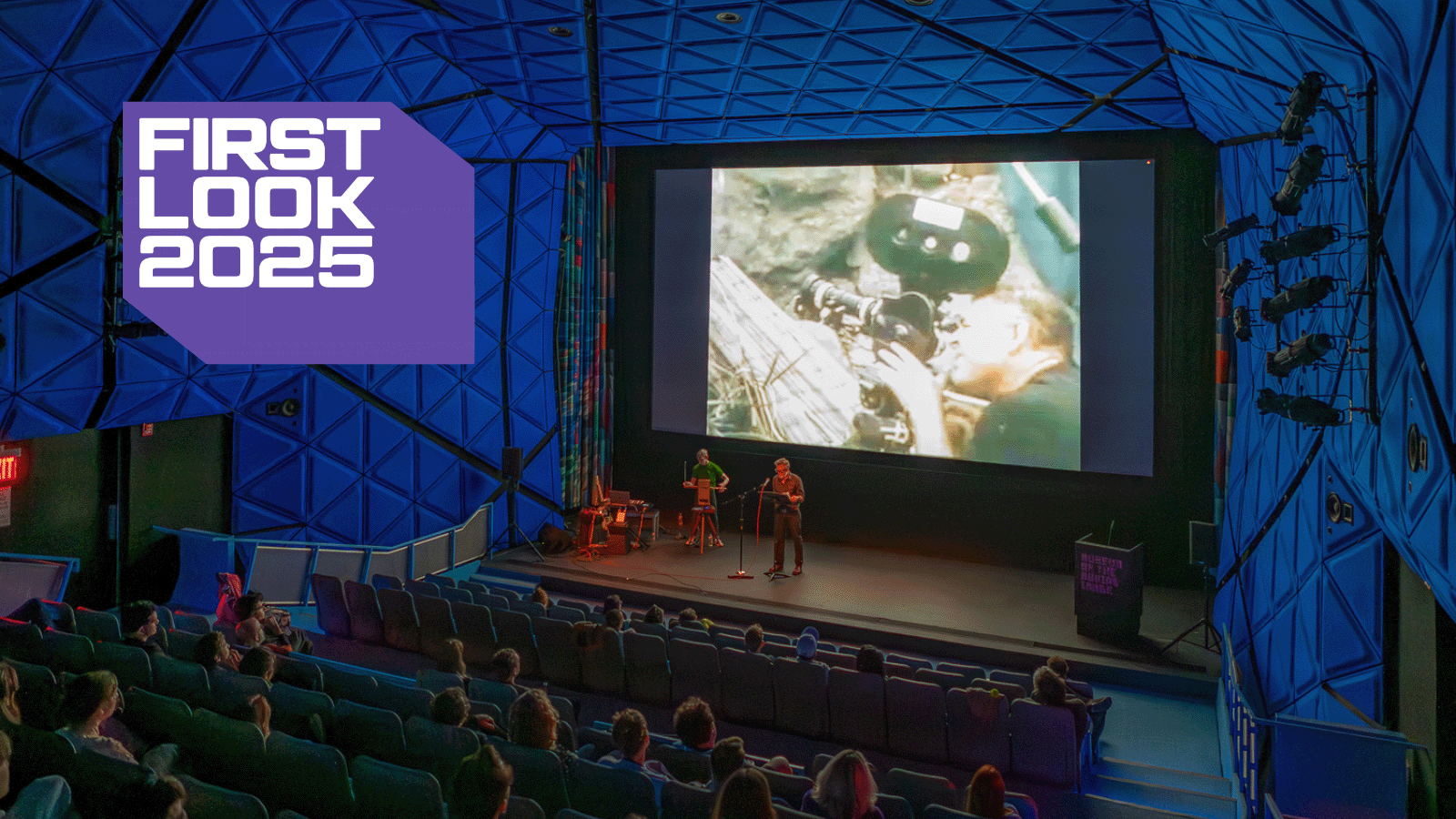 A purple boxy logo noting First Look 2025 is overlaid on top of an image of a blue-walled movie theater with a bright image on screen and figures on stage in front of an audience