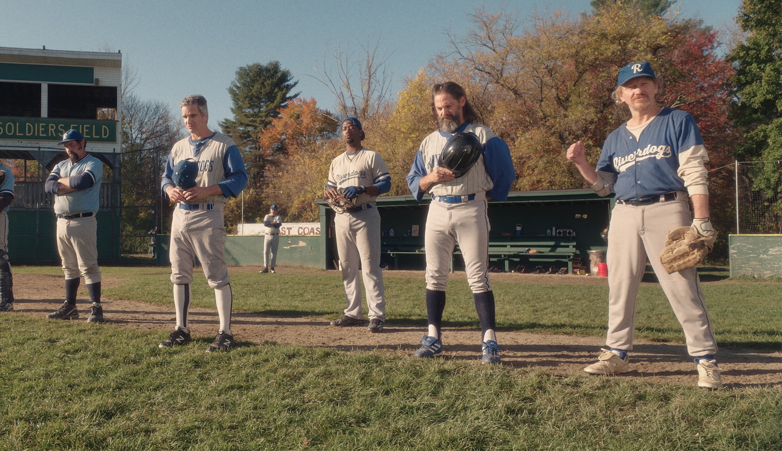 Minor league baseball players stand in a field pensively before a game, hats on hearts.