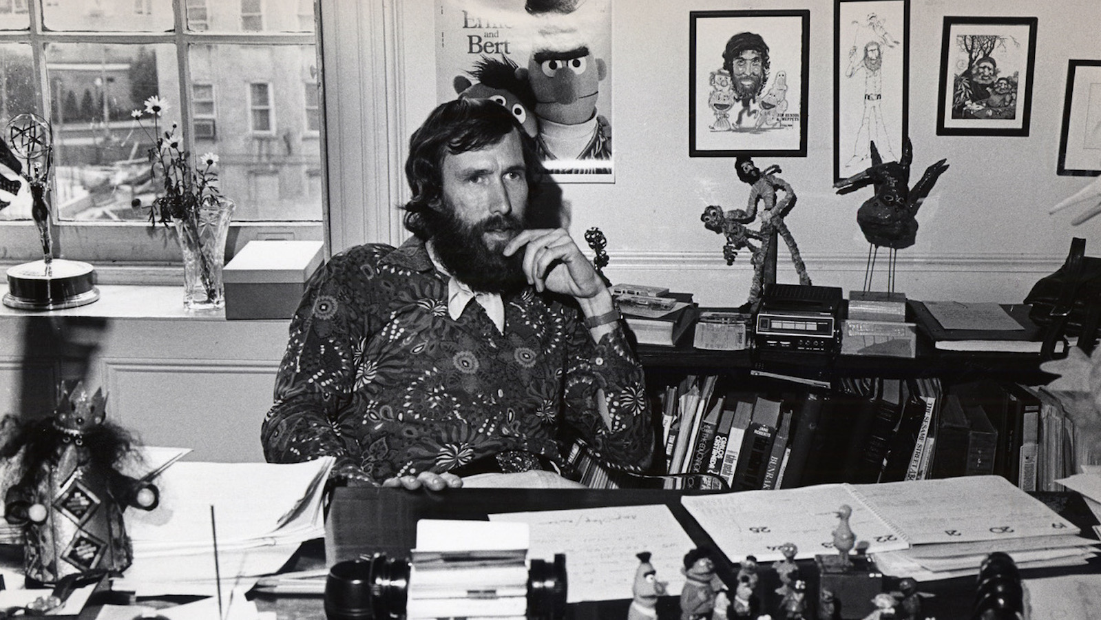 A bearded man sits at a desk talking on a phone is a black and white photo from the 1970s