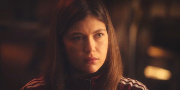 A young woman with long brown hair and wearing a track suit looks perturbed
