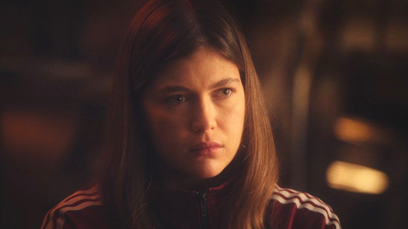 A young woman with long brown hair and wearing a track suit looks perturbed