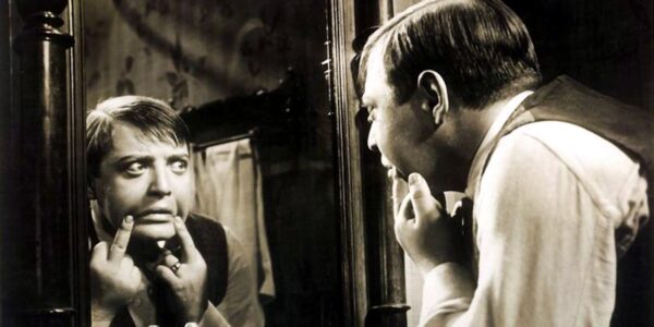 A man looks in a mirror making strange funny faces by pulling down the sides of his lips.