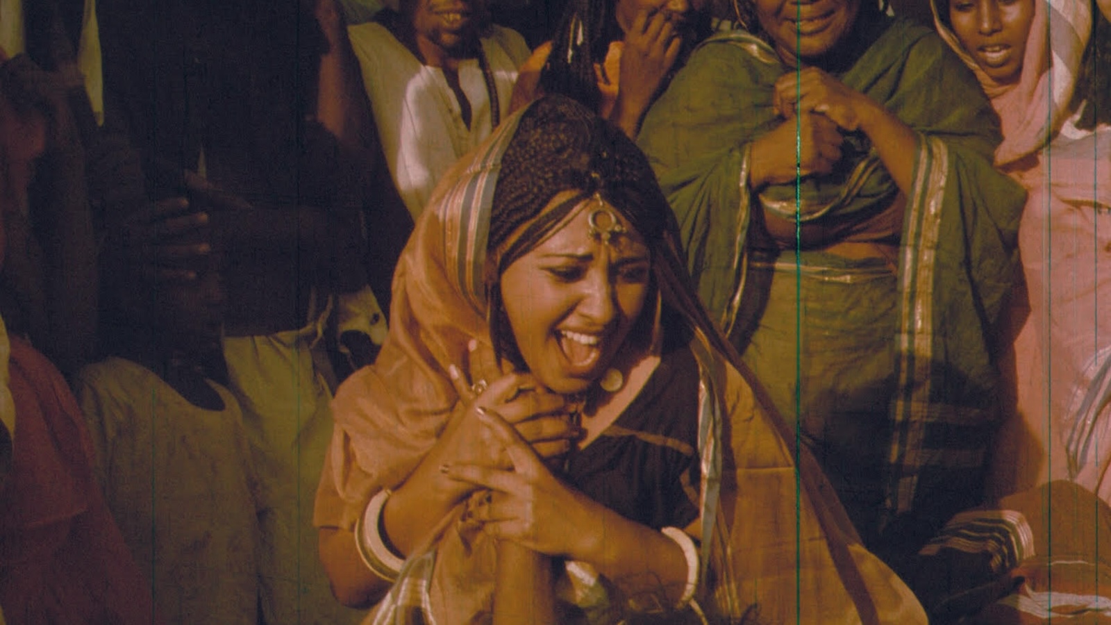 tajouje A woman in a sari screams with her mouth open, holding another person's hand as other women in saris stand around her.