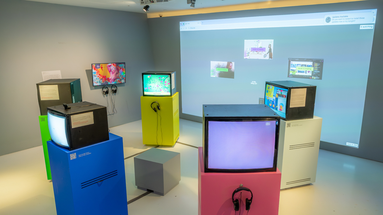 Thing + You event 1600×900 color photo of a museum installation showing 5 tube televisions on pedestals arranged like Stonehenge in a circle. Behind them on a wall is a large projection showing an internet browser.