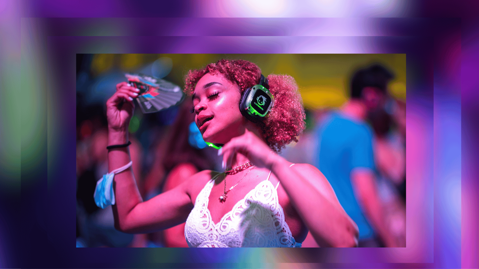 A young person wears headphones and holds a fan while dancing with eyes closed in a nightclub light atmosphere
