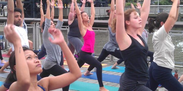 Women standing outside on a mat with their arms raised doing yoga.